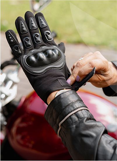 A person fastens a black motorcycle glove with a red motorcycle.
